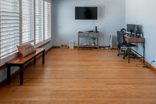 home office featuring light wood-style floors, baseboards, visible vents, and radiator heating unit