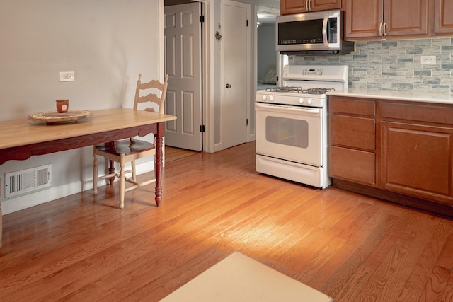 kitchen featuring stainless steel microwave, visible vents, white range with gas cooktop, light countertops, and brown cabinetry