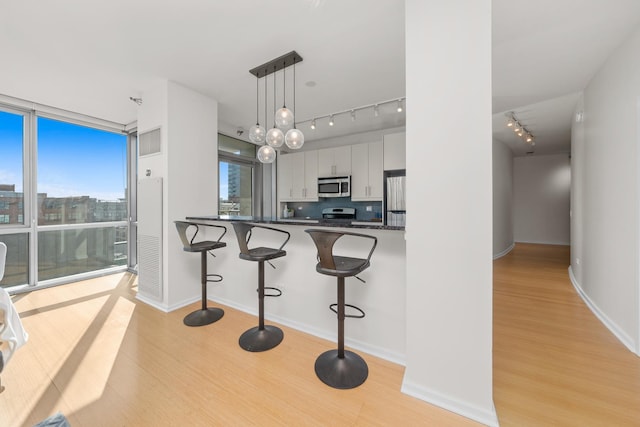 kitchen featuring a peninsula, light wood-style floors, hanging light fixtures, appliances with stainless steel finishes, and dark countertops