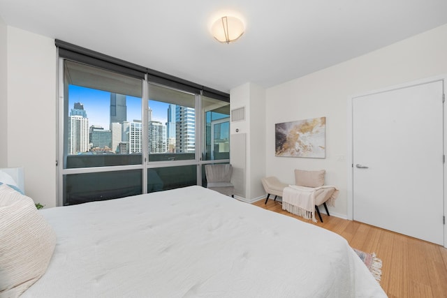 bedroom featuring a view of city, visible vents, wood finished floors, a wall of windows, and baseboards