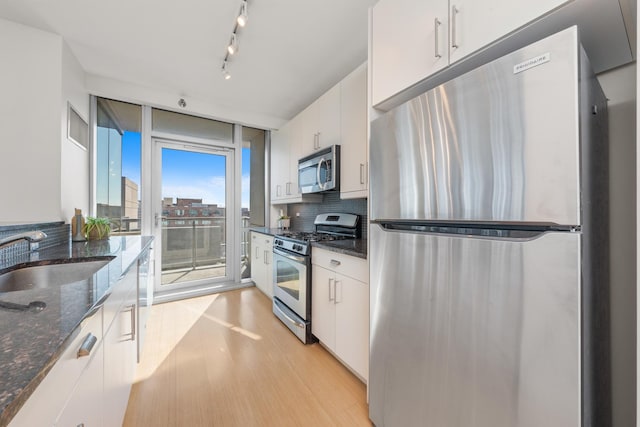 kitchen with dark stone countertops, white cabinetry, stainless steel appliances, and a sink