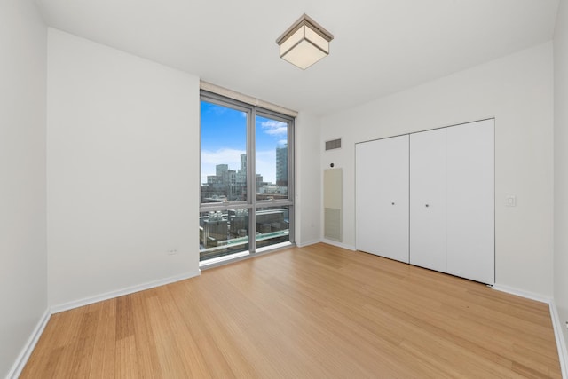 unfurnished bedroom with baseboards, visible vents, light wood-style flooring, a wall of windows, and a city view