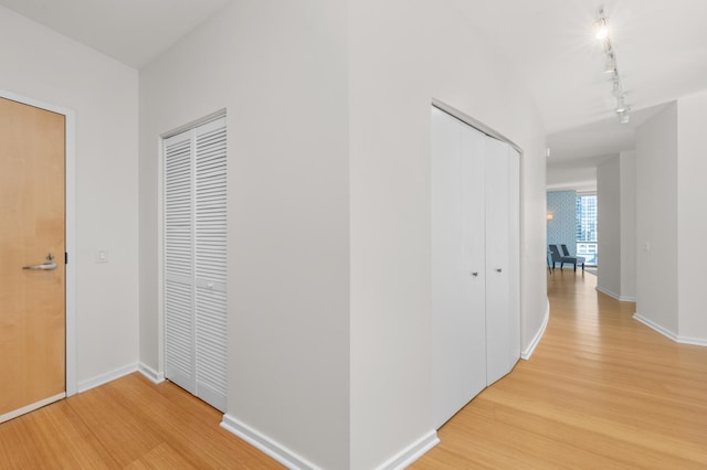 hallway featuring light wood-style floors, baseboards, and rail lighting