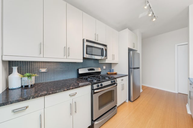 kitchen with decorative backsplash, dark stone counters, stainless steel appliances, light wood-type flooring, and white cabinetry