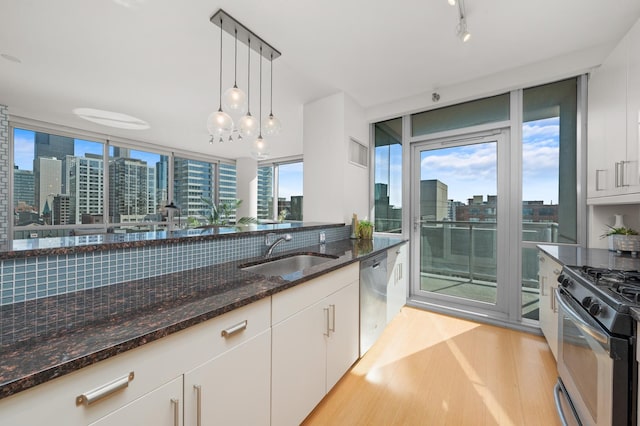 kitchen featuring dark stone countertops, decorative light fixtures, a view of city, white cabinetry, and a sink