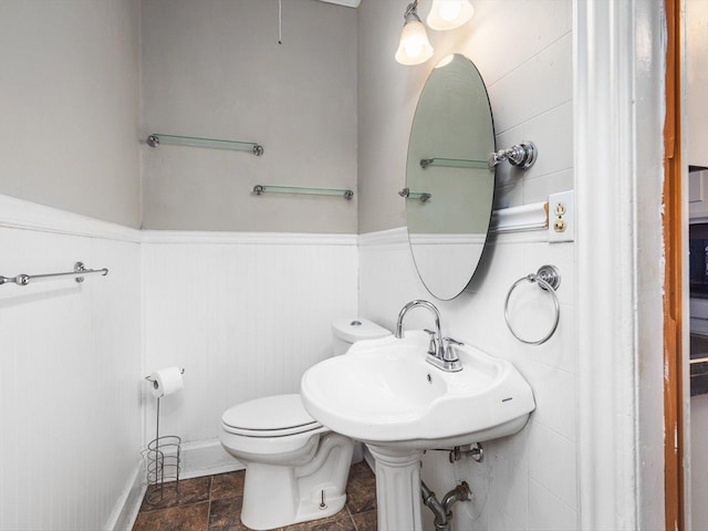 half bathroom with stone finish flooring, wainscoting, and toilet