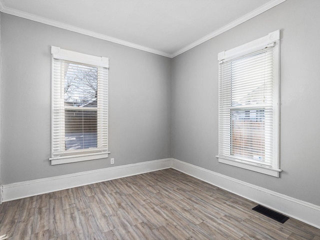 unfurnished room featuring crown molding, wood finished floors, visible vents, and baseboards