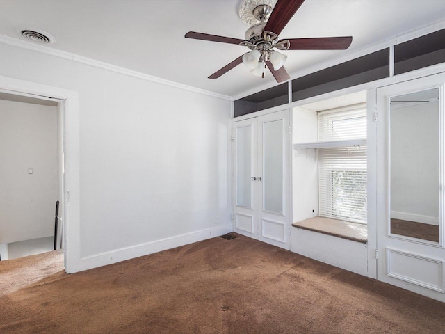 carpeted spare room with baseboards, visible vents, ceiling fan, and crown molding