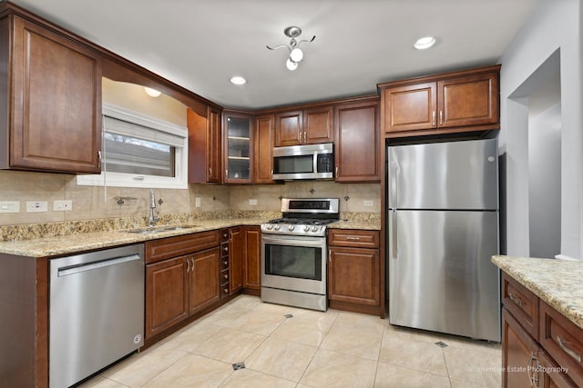 kitchen with light tile patterned floors, light stone counters, a sink, appliances with stainless steel finishes, and backsplash