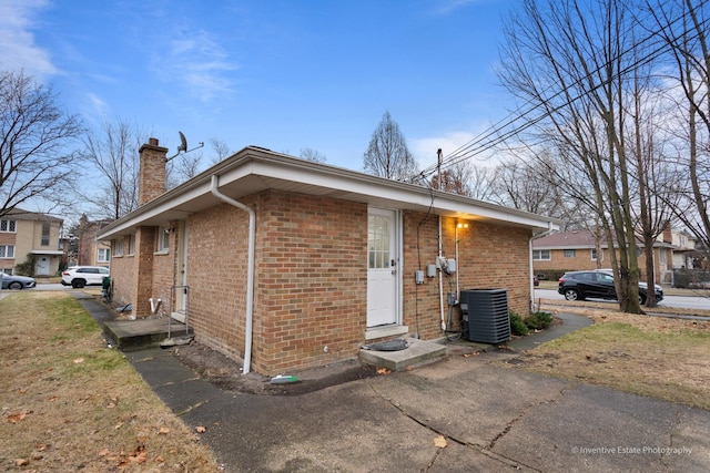 view of home's exterior with central air condition unit, entry steps, a chimney, and brick siding