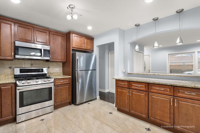 kitchen with appliances with stainless steel finishes, light stone countertops, decorative light fixtures, and decorative backsplash