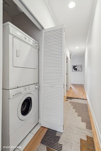 laundry room featuring stacked washer and dryer, laundry area, baseboards, ornamental molding, and light wood-type flooring