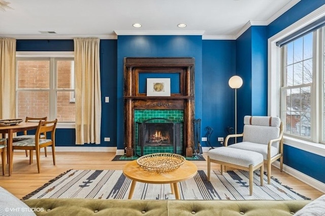 living area with baseboards, visible vents, a tile fireplace, ornamental molding, and wood finished floors