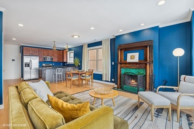 living area with recessed lighting, baseboards, a lit fireplace, light wood-type flooring, and crown molding