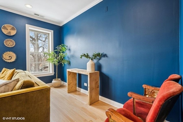 living area featuring baseboards, visible vents, ornamental molding, and wood finished floors