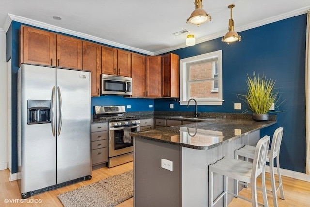 kitchen featuring pendant lighting, stainless steel appliances, ornamental molding, light wood-type flooring, and a peninsula