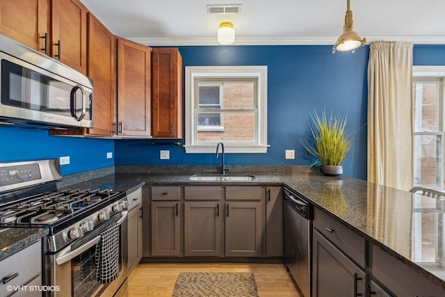 kitchen featuring pendant lighting, stainless steel appliances, visible vents, a sink, and dark stone counters