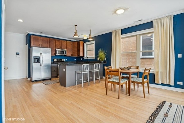 kitchen with a breakfast bar, crown molding, stainless steel appliances, dark countertops, and light wood-style flooring