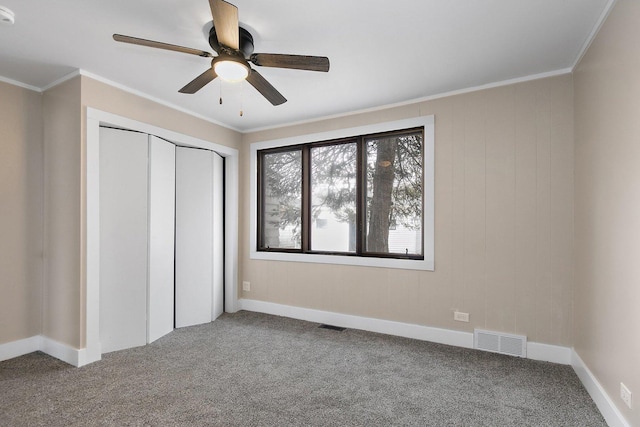 unfurnished bedroom featuring a ceiling fan, visible vents, a closet, carpet, and crown molding