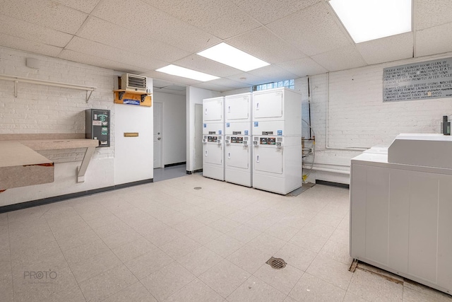 common laundry area featuring brick wall, stacked washer / dryer, washing machine and dryer, and light floors