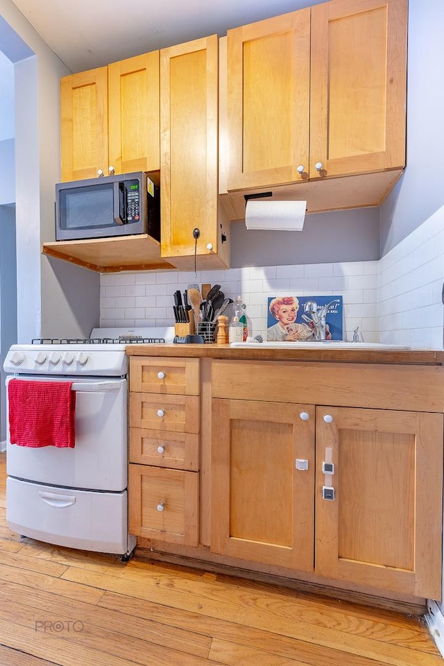 kitchen featuring white stove, tasteful backsplash, light countertops, and light wood-style floors