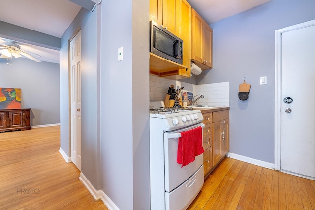 kitchen with white range with gas cooktop, stainless steel microwave, light countertops, light wood-type flooring, and backsplash