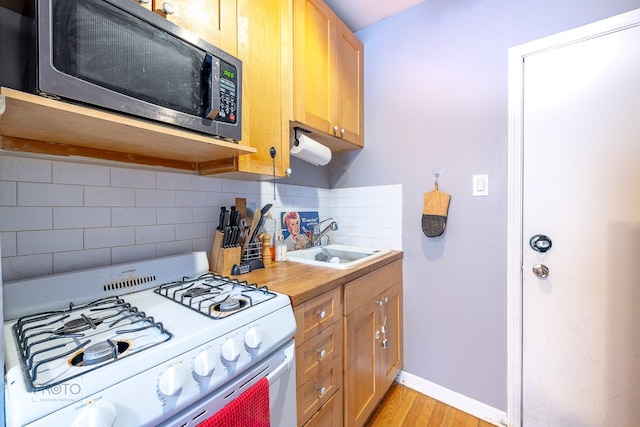 kitchen featuring a sink, light wood-type flooring, decorative backsplash, stainless steel microwave, and white gas range