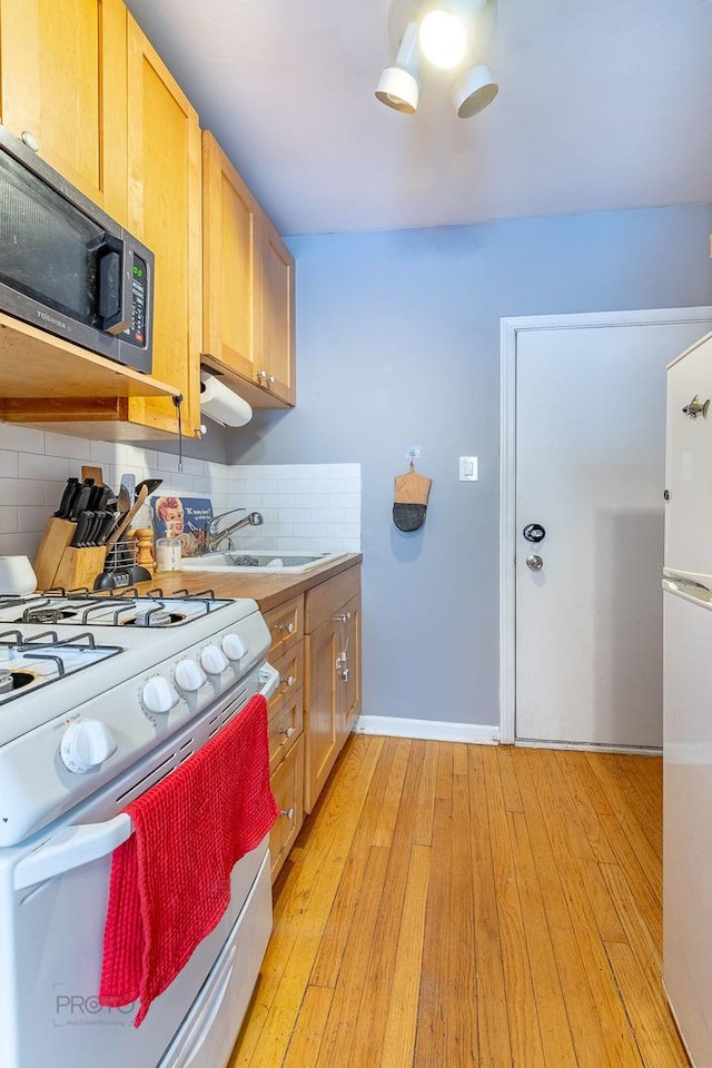 kitchen featuring white appliances, tasteful backsplash, light countertops, light wood-type flooring, and a sink