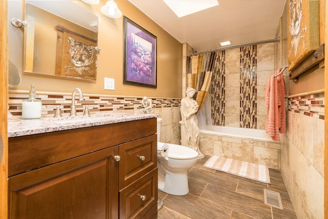 bathroom with tiled shower / bath, tile walls, visible vents, toilet, and vanity