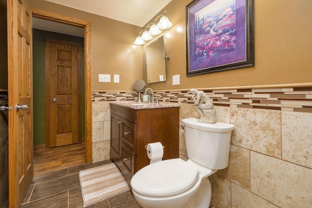 bathroom featuring a wainscoted wall, tile walls, toilet, wood tiled floor, and vanity