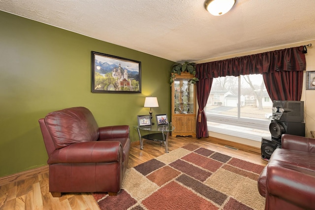 sitting room featuring visible vents, a textured ceiling, baseboards, and wood finished floors