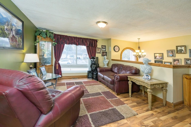 living room with a notable chandelier, a textured ceiling, baseboards, and wood finished floors