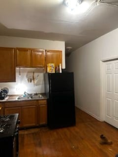 kitchen featuring dark wood-style floors, brown cabinets, a sink, and freestanding refrigerator