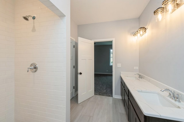 full bath featuring a tile shower, double vanity, a sink, and baseboards