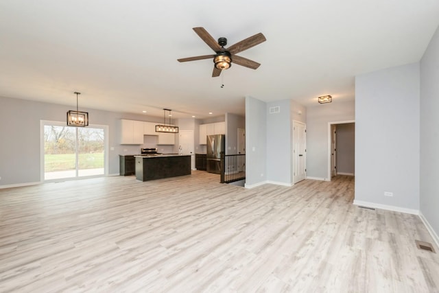 unfurnished living room with ceiling fan with notable chandelier, light wood finished floors, visible vents, and baseboards