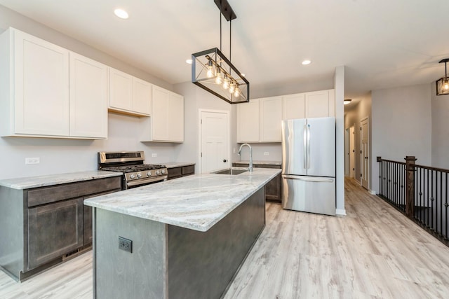 kitchen featuring light stone counters, stainless steel appliances, white cabinetry, a sink, and light wood-type flooring