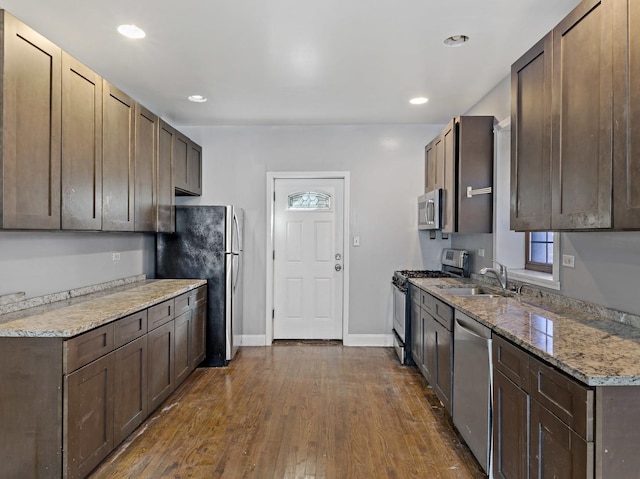 kitchen with stainless steel appliances, dark wood-style flooring, a sink, and light stone countertops