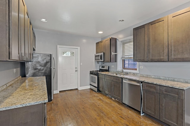 kitchen featuring stainless steel appliances, light wood-type flooring, a sink, and light stone counters