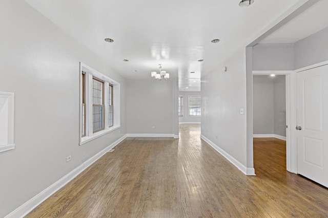 empty room with a notable chandelier, baseboards, and wood finished floors