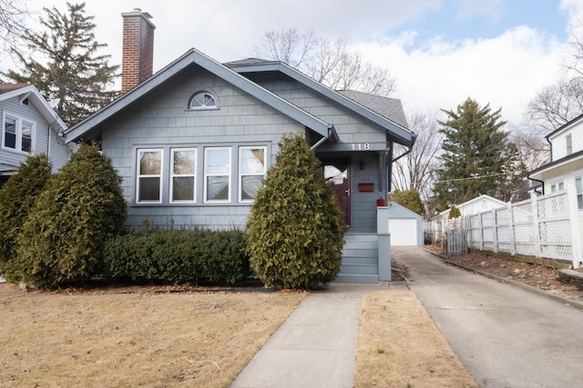 bungalow-style house featuring an outbuilding, a chimney, fence, and a garage