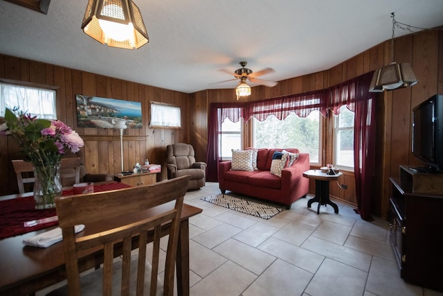 living area featuring light tile patterned floors, wooden walls, and a ceiling fan