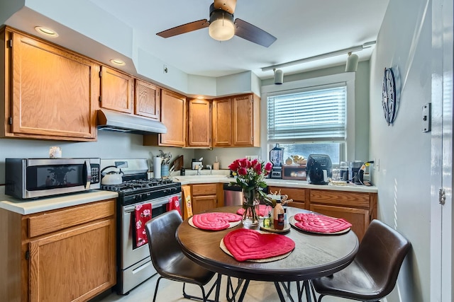 kitchen featuring brown cabinetry, a ceiling fan, appliances with stainless steel finishes, light countertops, and under cabinet range hood