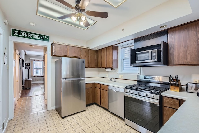 kitchen featuring light countertops, appliances with stainless steel finishes, a sink, ceiling fan, and baseboards