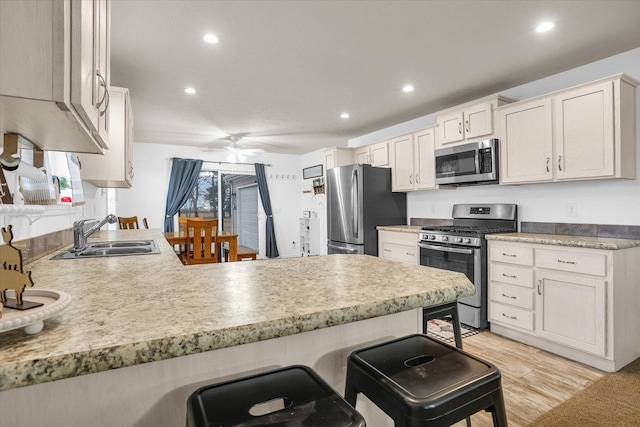 kitchen featuring a breakfast bar, light wood finished floors, appliances with stainless steel finishes, a sink, and a peninsula