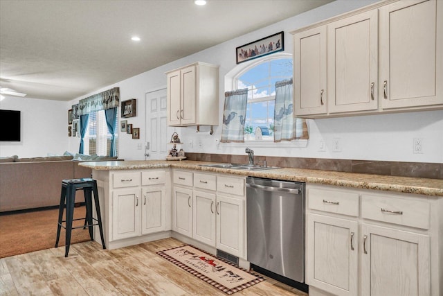 kitchen featuring a peninsula, a sink, open floor plan, stainless steel dishwasher, and a wealth of natural light