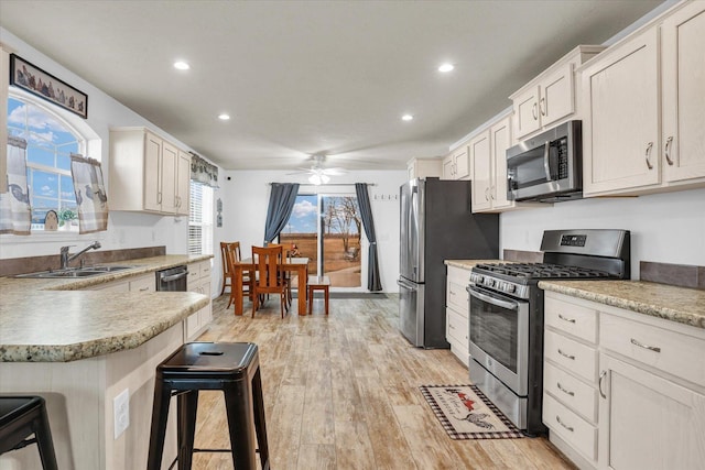 kitchen with a breakfast bar, light countertops, light wood-style flooring, appliances with stainless steel finishes, and a sink