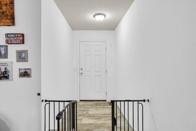 hall featuring a textured ceiling, an upstairs landing, and light wood-style floors