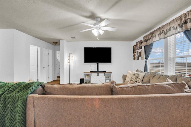 living room with ceiling fan, visible vents, and a textured ceiling