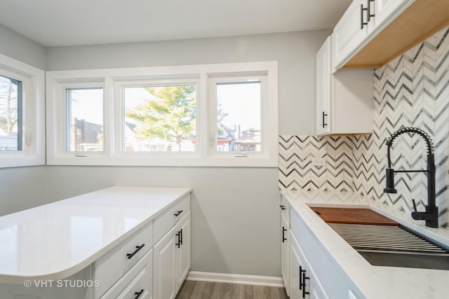 kitchen featuring tasteful backsplash, baseboards, light stone countertops, white cabinetry, and a sink