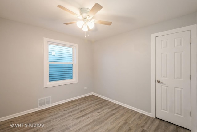 spare room featuring baseboards, visible vents, ceiling fan, and wood finished floors